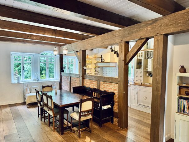 Helles Esszimmer mit einem großen Holztisch und offenen Küchenbereich aus Holz.