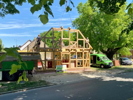 Rohbau eines Hauses mit Holzgerüst, Handwerker arbeiten unter blauem Himmel.