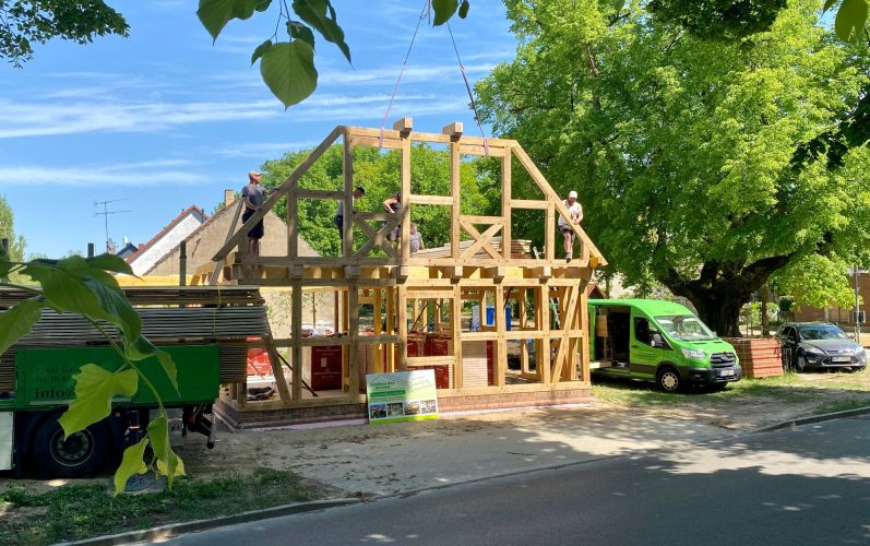 Fachwerkhaus- Entwurf: Christianus_und_Paulsen Beratende Ingenieure Fachwerkhaus mit rotem Satteldach, umgeben von Bäumen und einem Gehweg.