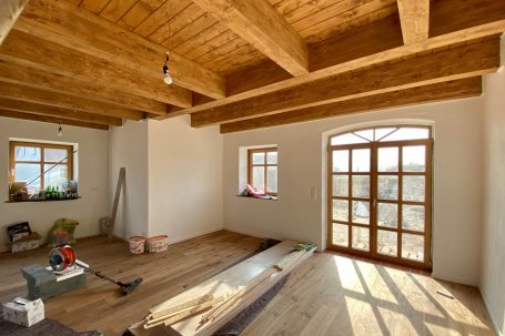 Helle, leerstehende Räume mit Holzdecken und Fenstern, teilweise Renovierungsarbeiten.