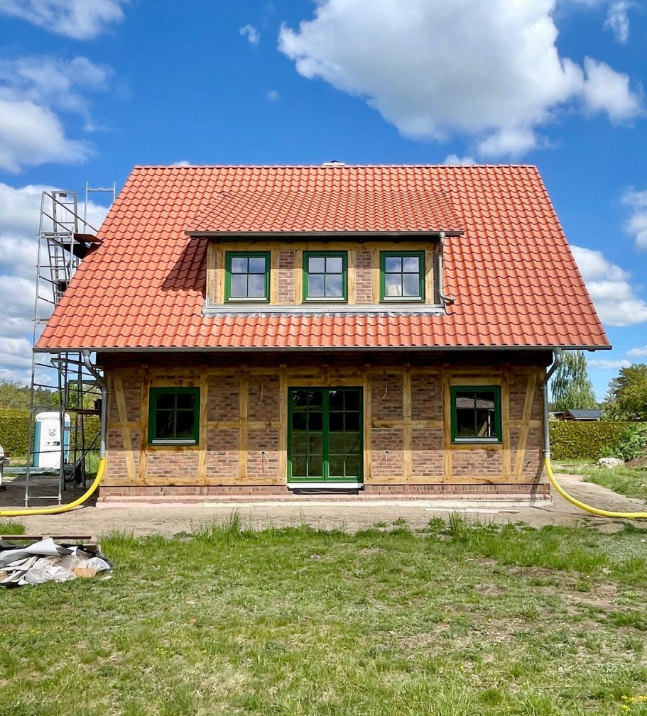 Fachwerkhaus mit rotem Dach und grünem Fensterrahmen, umgeben von Wiese.