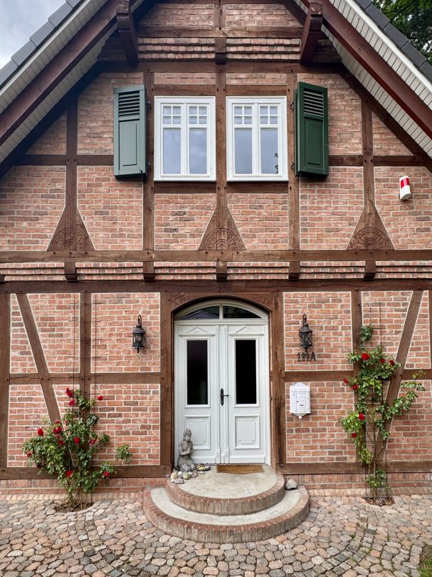 Traditionelles Fachwerkhaus mit roten Ziegeln, weißen Fenstern und grünen Fensterläden.