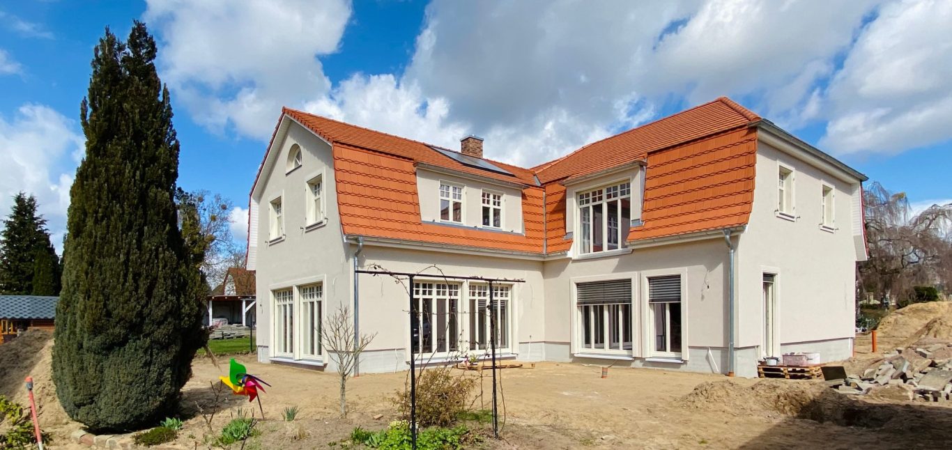 Moderne zweigeschossige Villa mit rotem Dach und Garten, umgeben von Bäumen.