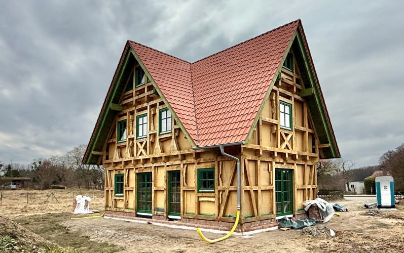 Neu gebautes, traditionell gerichtetes Fachwerkhaus  mit roten Dachziegeln und grünen Fensterrahmen.