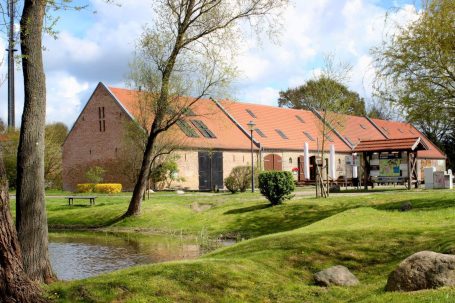 Ländliches Haus mit roten Dächern, umgeben von Bäumen und einem kleinen Teich.
