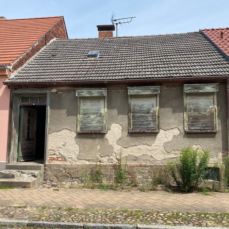 Verlassenes, verfallenes Haus mit teilweise abgeblättertem Putz und verdorrten Pflanzen.