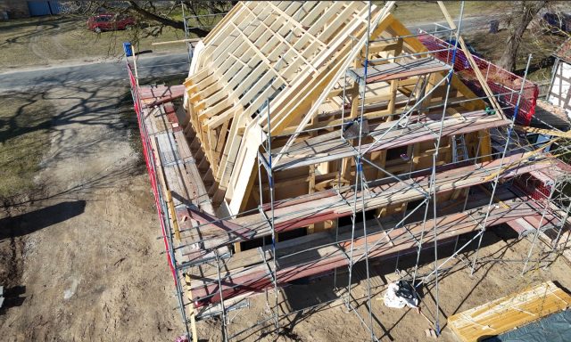 Unfertiges Gebäude mit Holzrahmen und Gerüst in einer ländlichen Umgebung.