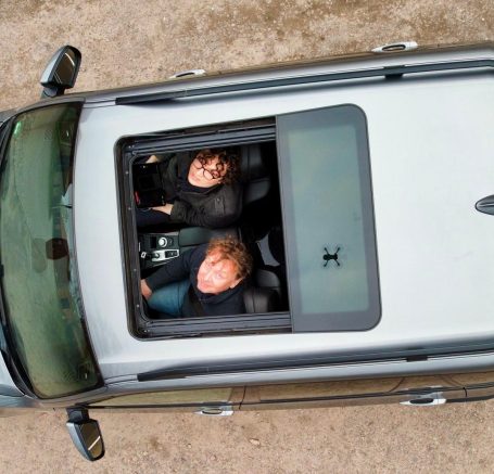 Zwei Personen sitzen in einem grauen Auto und schauen nach oben.