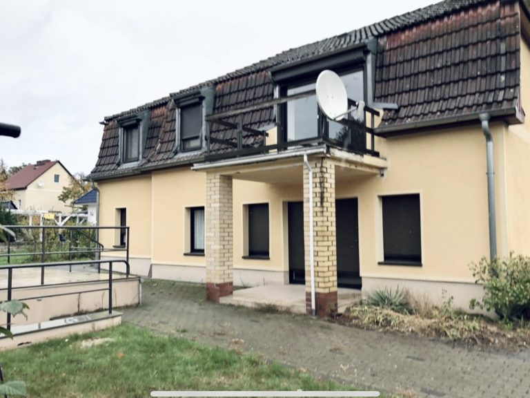 Zweistöckiges Wohnhaus mit Satellitenschüssel und begrüntem Vorgarten.