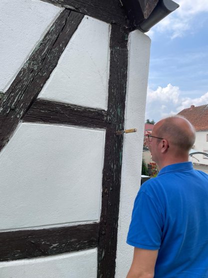Mann in blauer Kleidung betrachtet eine Fachwerkstruktur an einer Wand.