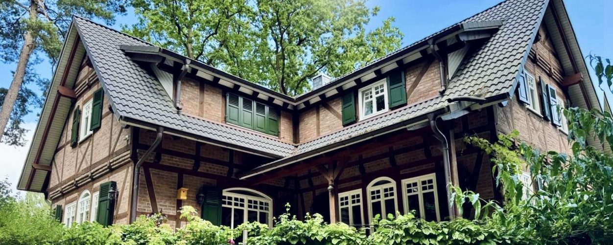 Fachwerkhaus mit grünem Garten und Bäumen im Hintergrund, helles Wetter.