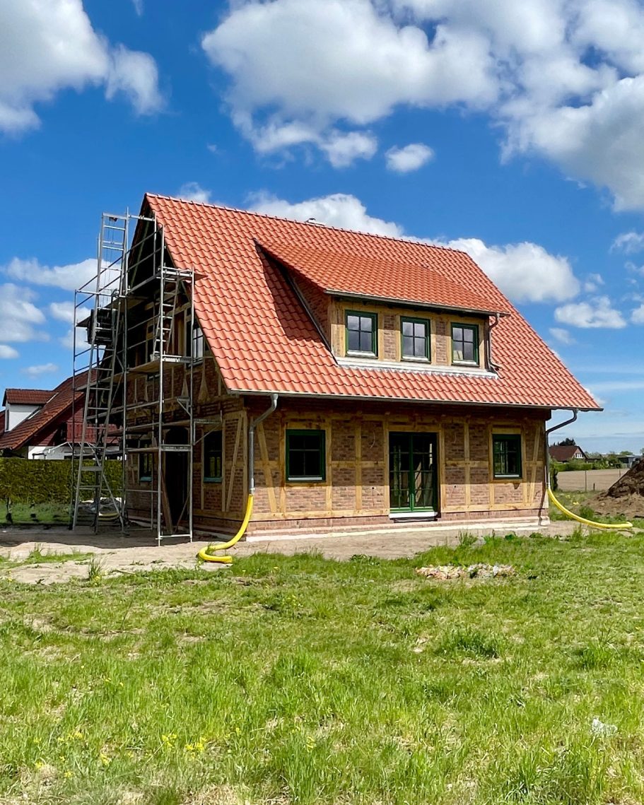 Neues Fachwerkhaus im Bau mit Gerüst und grünem Rasen unter blauem Himmel.
