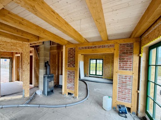 Innenansicht eines Rohbaus mit Holzrahmen und Ziegelwänden, Fenster ohne Verglasung.