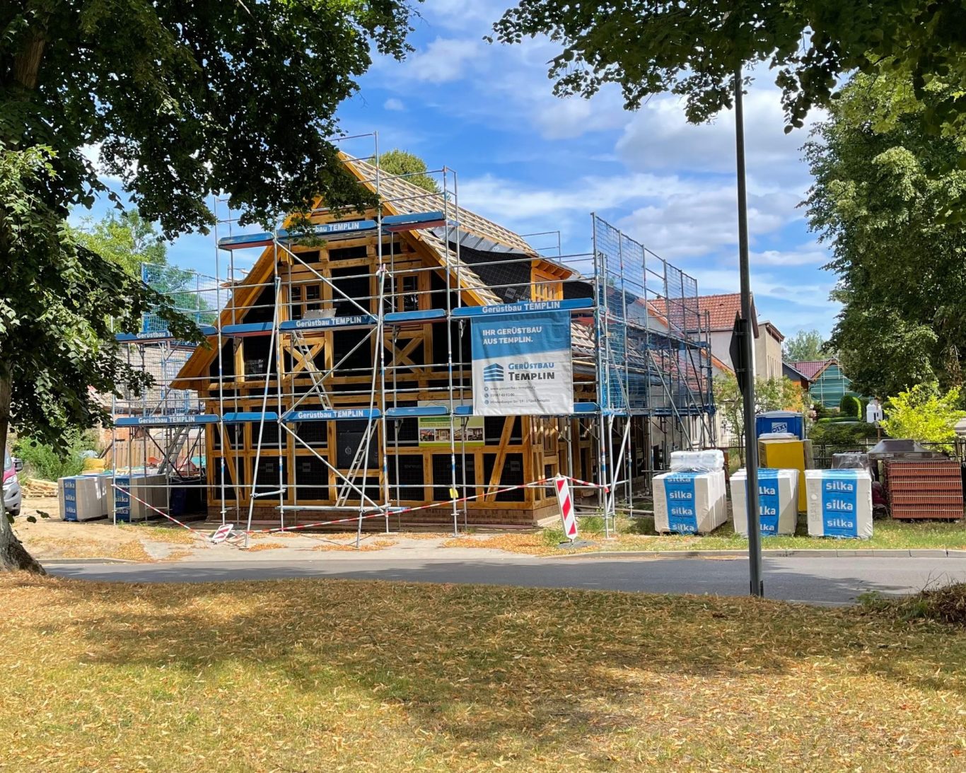 Entwurf @Christianus_und_Paulsen Beratende Ingenieure Baustelle eines Hauses mit Gerüst und Bauzubehör, umgeben von Bäumen und Wiese.