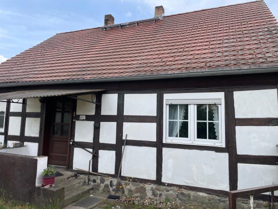 Fachwerkhaus mit rotem Dach, weißen Wänden und braunem Eingang.