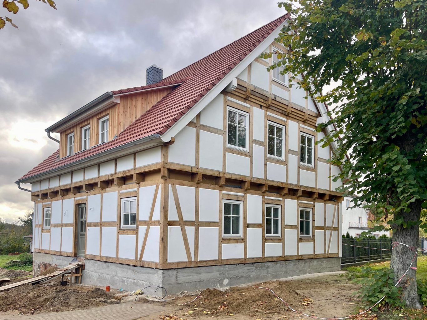 Fachwerkhaus mit hellem Putz mit rot gedecktem Dach und Blick auf einen Baum im Vordergrund.